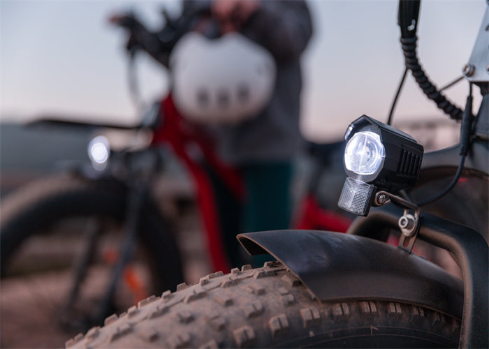 Close-up of a TESWAY S7 electric bike's front light, with a blurred background of a rider holding a helmet